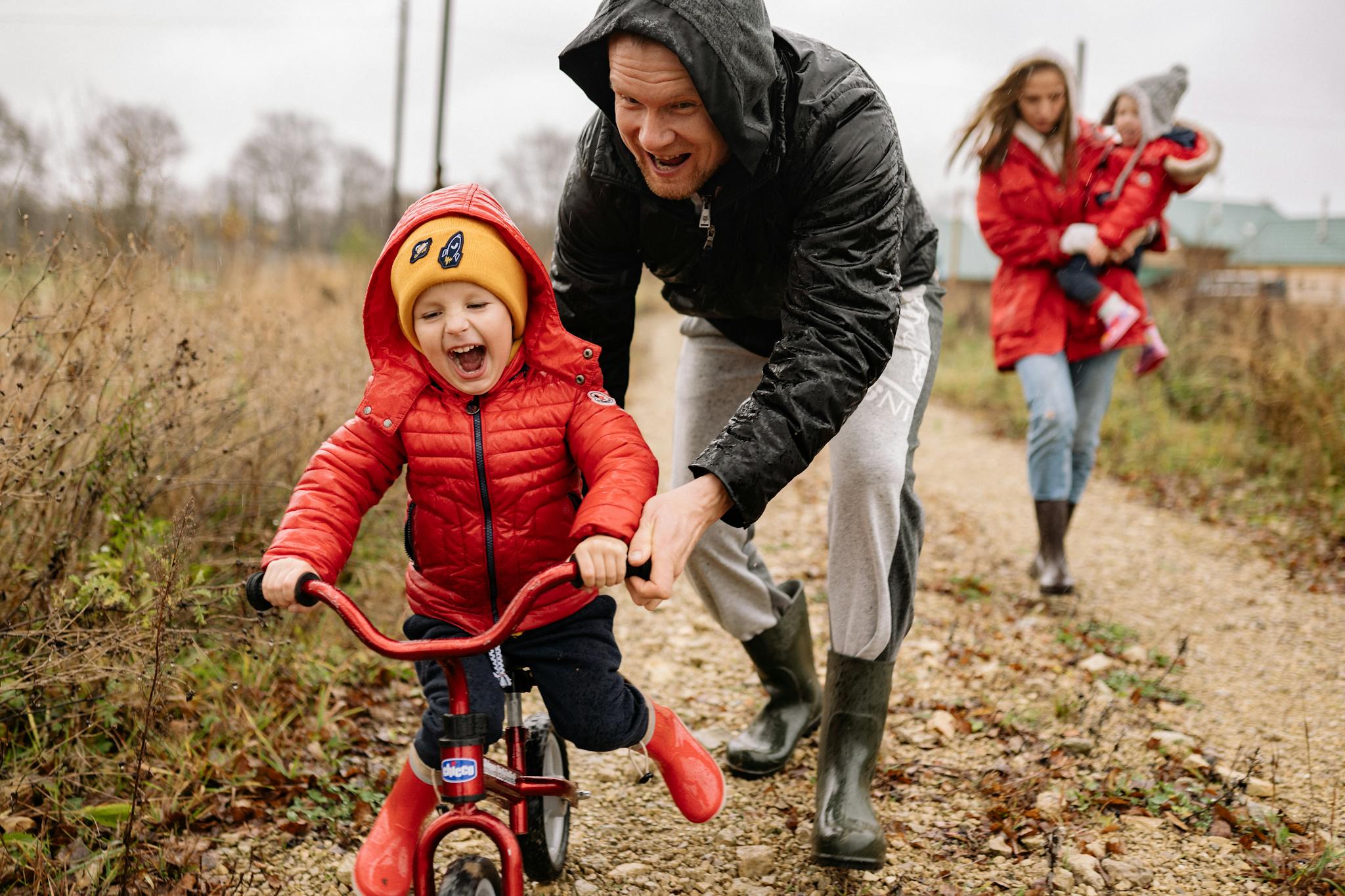 Father helping son ride a bicycle on a fall day while mother and daughter watch.